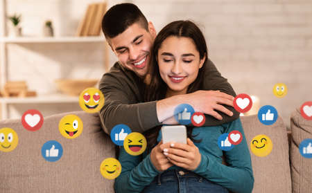 Smiling millennial european man hugging woman and looking at phone on social networks