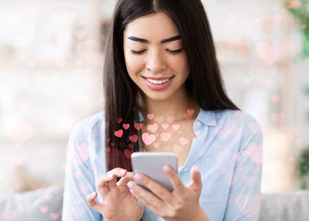 Smiling young asian female has romantic chat with boyfriend on smartphone or social networkの写真素材