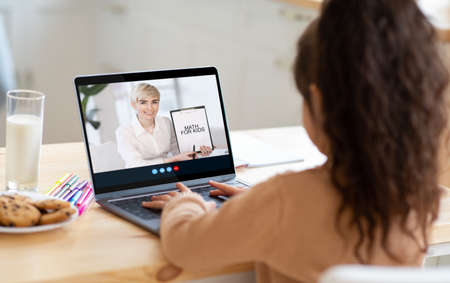 Little girl student have video call with adult caucasian woman teacher, math lesson on laptop screen at homeの写真素材