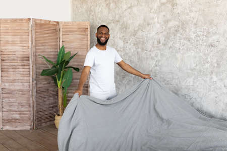Satisfied young African American man making bedの写真素材