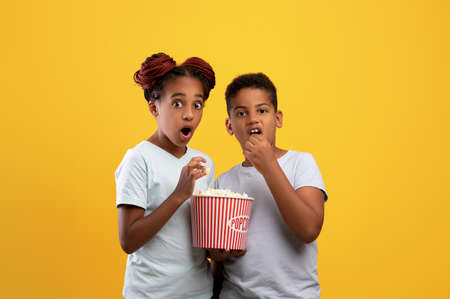 Emotional black kids boy and girl eating popcorn, watching movieの写真素材
