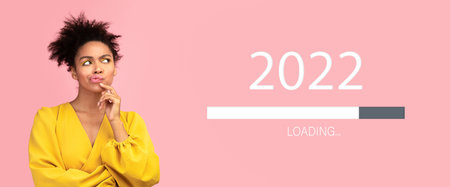 Thoughtful black woman looking at 2022 loading bar, waiting for upcoming New Year on pink studio background, collageの写真素材