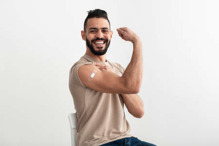 Young Arab man with adhesive bandage getting vaccinated against covid-19, demonstrating his muscles on white backgroundの写真素材