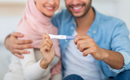 Muslim woman showing positive pregnancy test to camera, cuddling with her husband, selective focusの写真素材