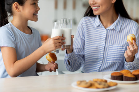 Time for vitamins. Asian girl and her young mother drinking milk in kitchen, enjoying calcium drink, closeup, cropの写真素材