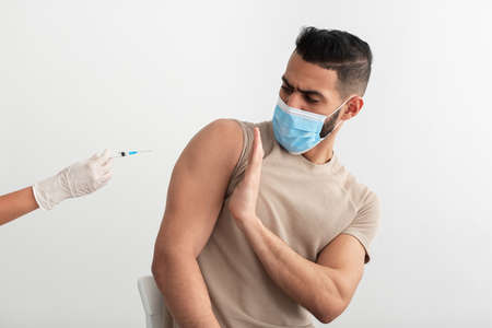 Young Arab guy in face mask stopping doctor from making covid vaccine injection, being against coronavirus immunizationの写真素材