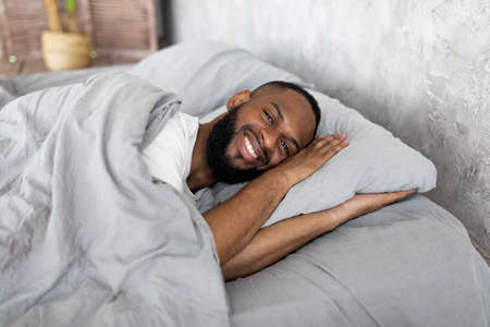 Young African American man lying in bed looking at cameraの写真素材