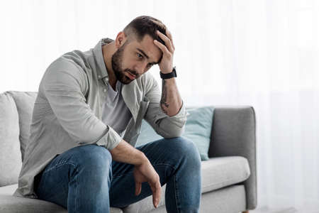 Man sit alone feeling sad worry regret or fear, depressed and desperate in sofa at homeの写真素材