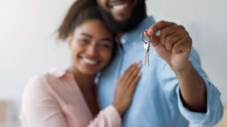 Satisfied millennial black couple hugging, showing keys to new apartment. Focus on keys to first own...