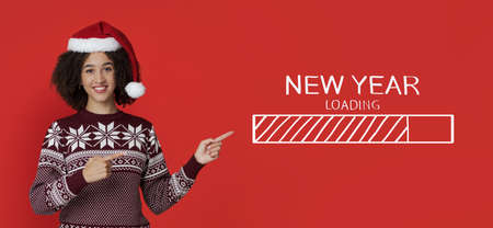 Loading New Year. Young Afro lady in warm sweater and Santa hat pointing fingers at processing bar,...
