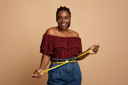 Cheerful african american slender woman measuring her waistの写真素材