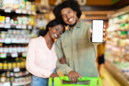 African American Buyers Couple Showing Smartphone Screen Standing In Supermarketの写真素材