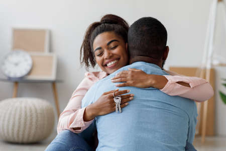 Happy millennial african american woman holding house keys, hugging boyfriend in their new apartmentの写真素材