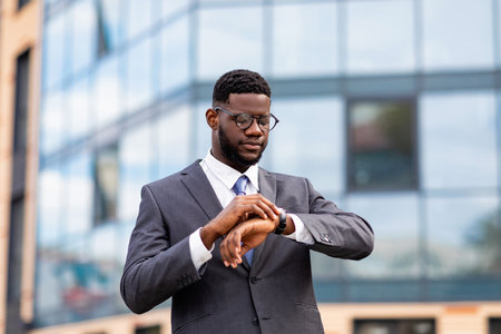 Successful african american CEO checking time on his wristwatch, walking during break in downtown areaの写真素材
