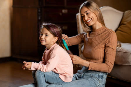 Loving smiling mom brushing her pretty daughters hairの写真素材