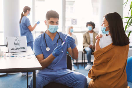 Male Doctor Taking Dose Of Covid-19 Vaccine For Asian Lady