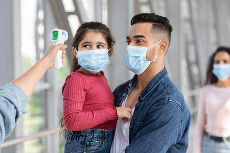 Safe Travels. Staff Checking Body Temperature For Father And Daughter At Airport