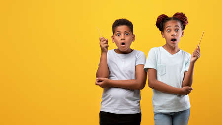 Excited black siblings showing eureka gesture on yellow