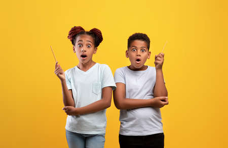 Amazed black girl and boy raising pencils upの写真素材