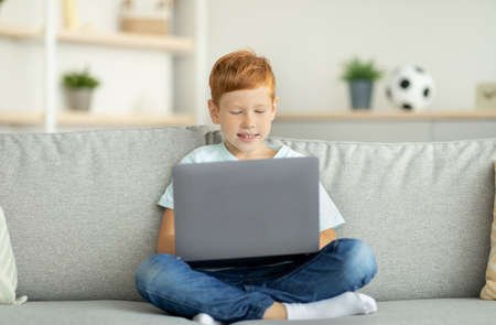 Redhead child using laptop, playing online video gameの写真素材