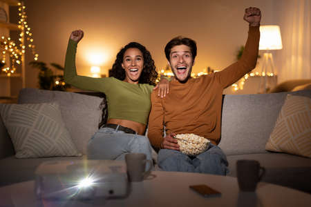 Couple Watching Sport Channel Using Projector Shaking Fists At Homeの写真素材