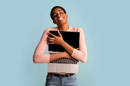 Portrait Of Happy Excited Black Woman Holding And Embracing Opened Laptopの写真素材