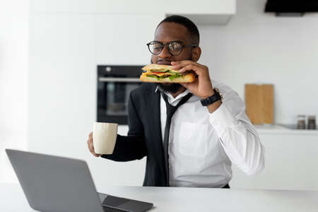 Black man rushing to work eating sandwich at homeの写真素材