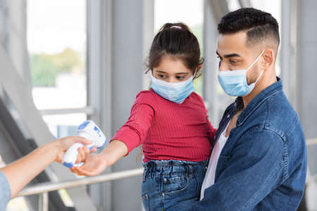 Pandemic Rules. Worker Checking Body Temperature For Father And Daughter At Airport