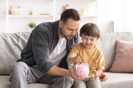 Early financial education. Cute little boy putting coin into piggy bank, daddy teaching his son to keep and safe moneyの写真素材