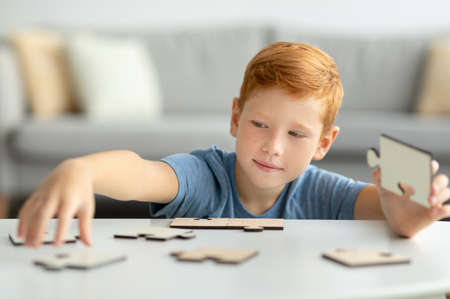 Smart redhead boy holding wooden puzzles, playing alone at homeの写真素材