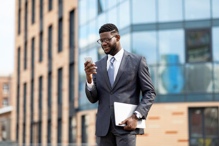 Happy african american entrepreneur checking emails on cellphone, having break, walking outdoorsの写真素材