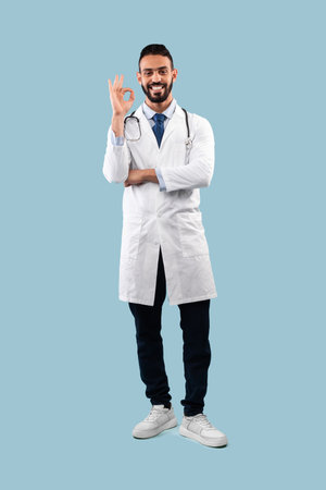 Cheerful Arabic Male Doctor Gesturing Okay Sign Over Blue Backgroundの写真素材