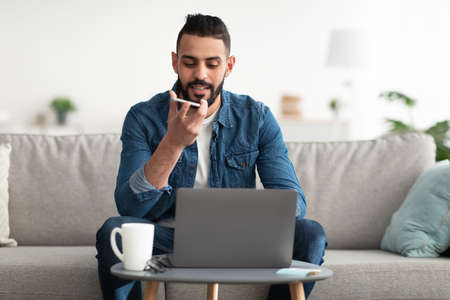 Freelancing, online job or education. Arab man using laptop computer and smartphone, having business meeting from homeの写真素材