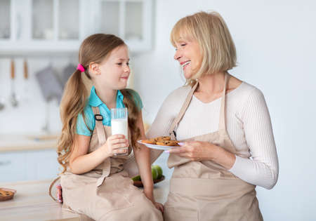 Grandma Feeding Cute Little Girl With Cookies And Milkの写真素材