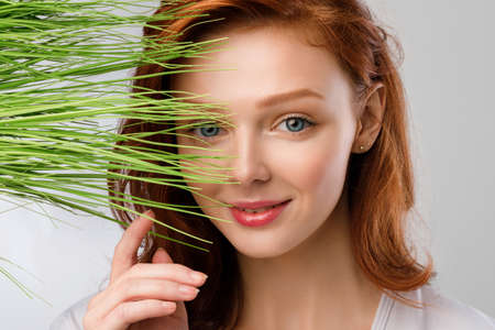 Ginger-Haired Girl Posing With Green Grass Near Face, Gray Backgroundの写真素材
