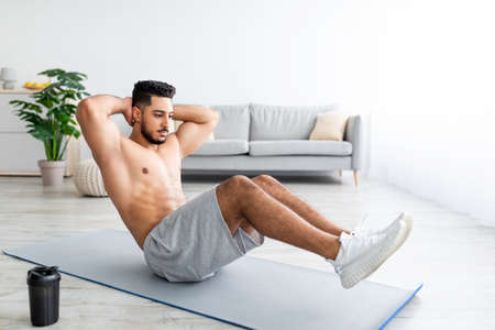 Full length of fit Arab man strengthening core muscles, doing abs exercises on mat at home