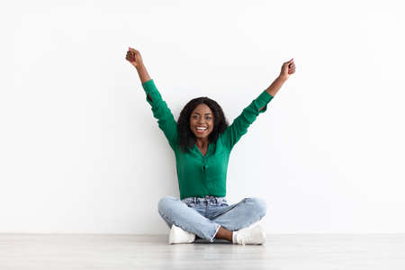 Emotional young black woman sitting on floor, raising hands upの写真素材