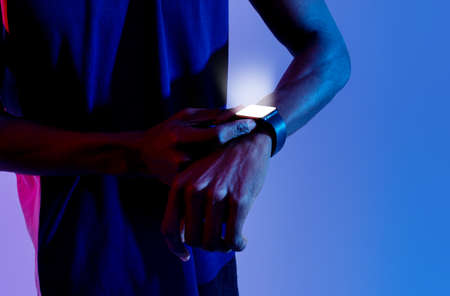 Unrecognizable young black sportsman checking his smartwatch with mockup for app on screen in neon lightの写真素材