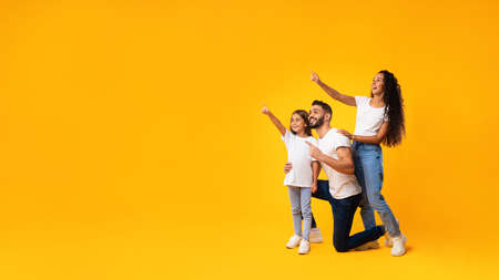 Excited Middle-Eastern Family Pointing Finger Aside Over Yellow Background, Panoramaの写真素材