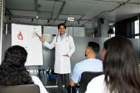 Cheerful man doctor standing next to presentation board, having speechの写真素材