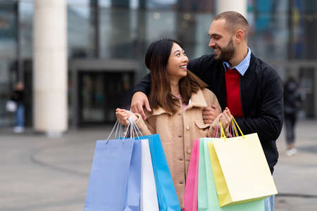 Shopping time, low price sales. Young international couple holding shopper bags, hugging near city mall, copy spaceの写真素材