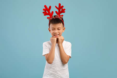 Making Wish. Little asian boy wearing xmas reindeer horns dreaming about somethingの写真素材