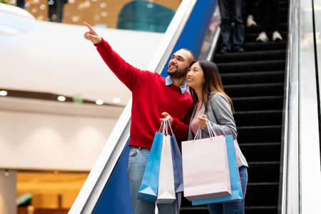 Young interracial couple shopping together in city mall, holding shopper bags, making purchases, copy spaceの写真素材