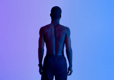 Back view of strong young black man with naked torso posing in neon lightの写真素材