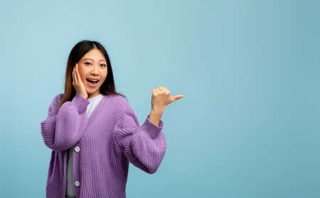 Omg, cool offer. Surprised asian lady pointing at copy space showing place for advert or promotional text, bannerの写真素材