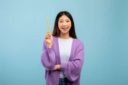 Wow, eureka. Asian female student having great idea, finding inspiration or solution to problem on blue backgroundの写真素材