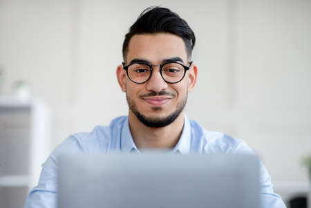 Millennial Arab businessman with laptop pc working online, having business meeting on webcam at modern officeの写真素材