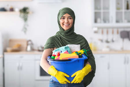 Cheerful young islamic housewife holding bucket with cleaning suppliesの写真素材