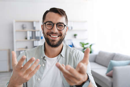 Smiling emotional adult european male with beard in glasses looks at camera and shooting video for blogの写真素材