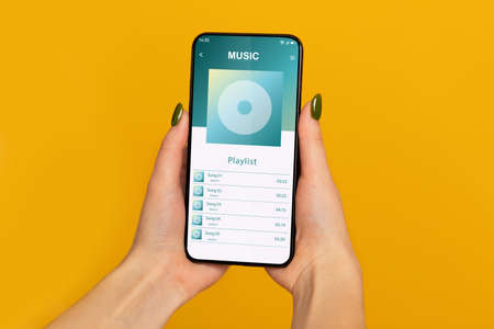 Female Hands Holding Smartphone With Opened Music Player Playlist On Screenの写真素材